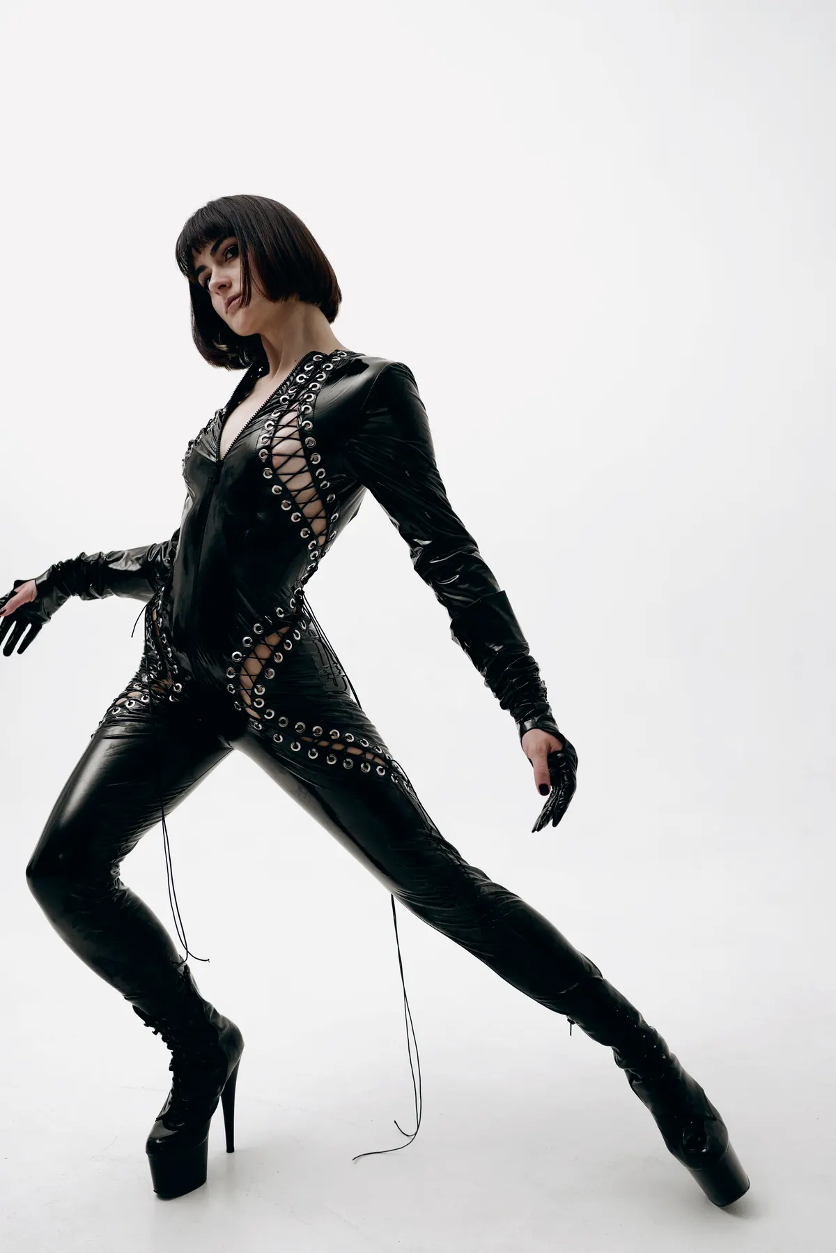A model strides in a laced leather catsuit and platform boots