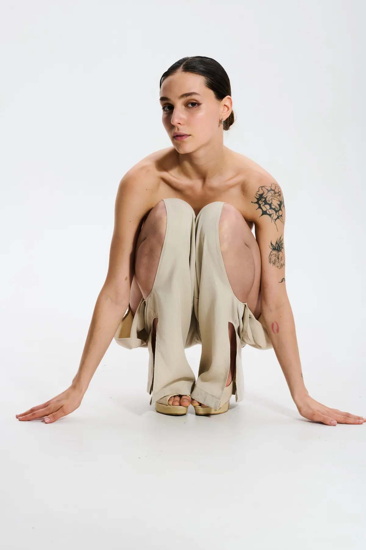 A model crouches in a cream corset and trousers, one hand flat on the floor